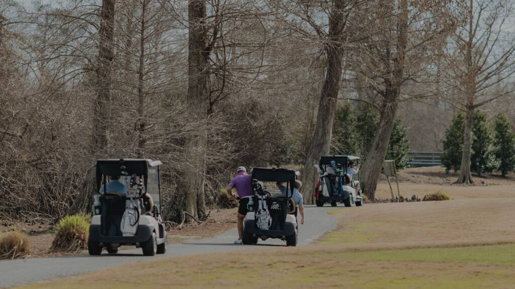 Golfers riding in a CGA-branded cart across fairway